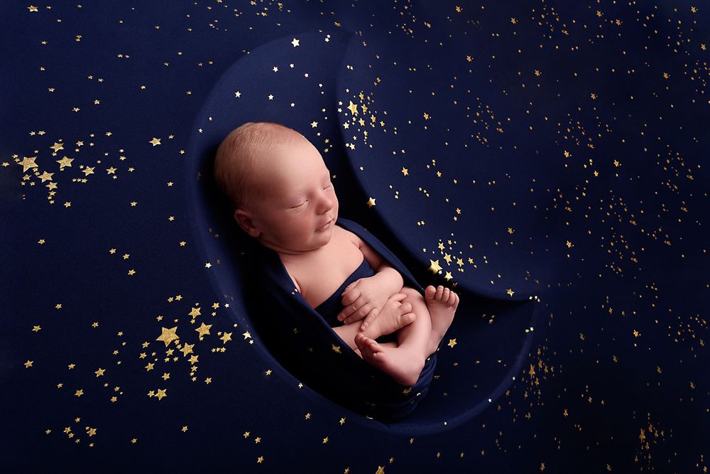 Sleeping newborn on dark blue backdrop with scattered gold stars.