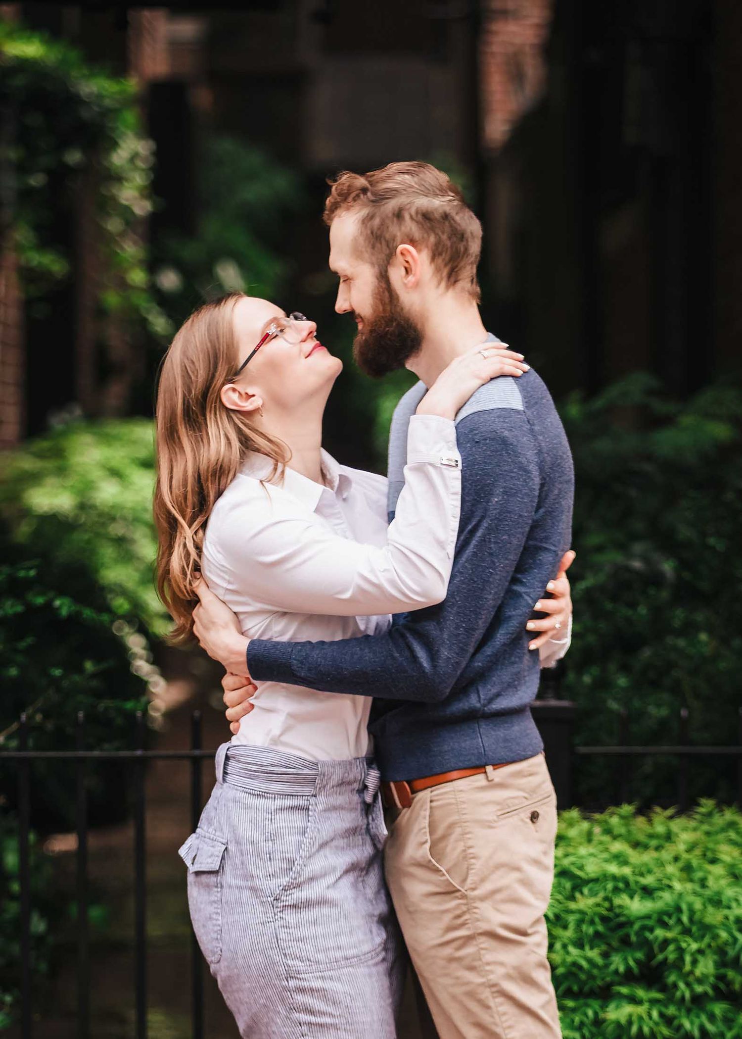 A close-up portrait of a couple embracing and smiling warmly at each other in a brick-lined Beacon Hill alleyway, framed by lush greenery.