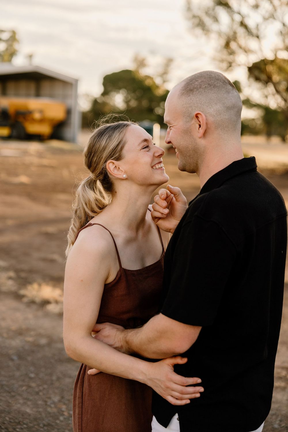 A couple shares intimate moments and laughter during a sunset photoshoot in brown and black outfits.