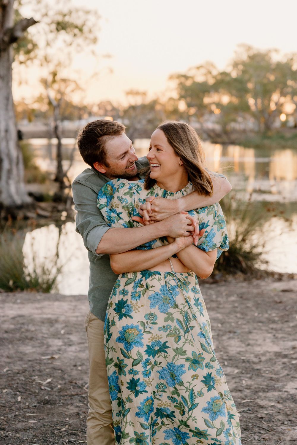 Couple in matching floral patterns share a joyful embrace by a waterfront at sunset.