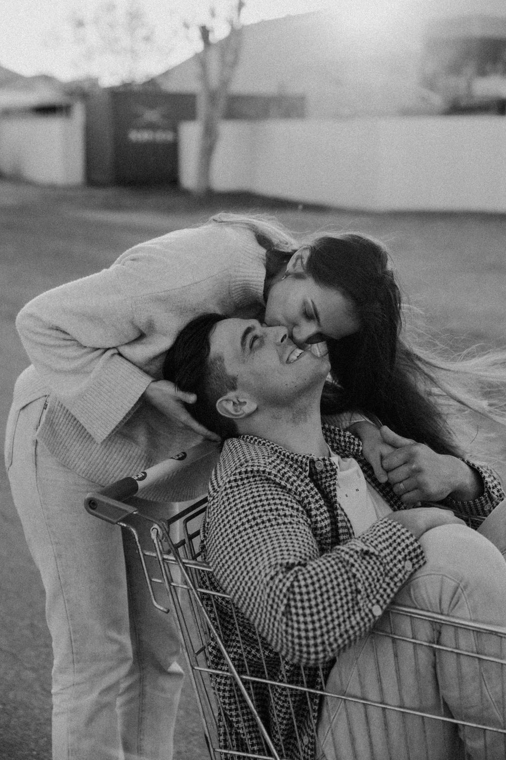A couple in black and white photograph sharing a tender kiss while leaning over a shopping cart.