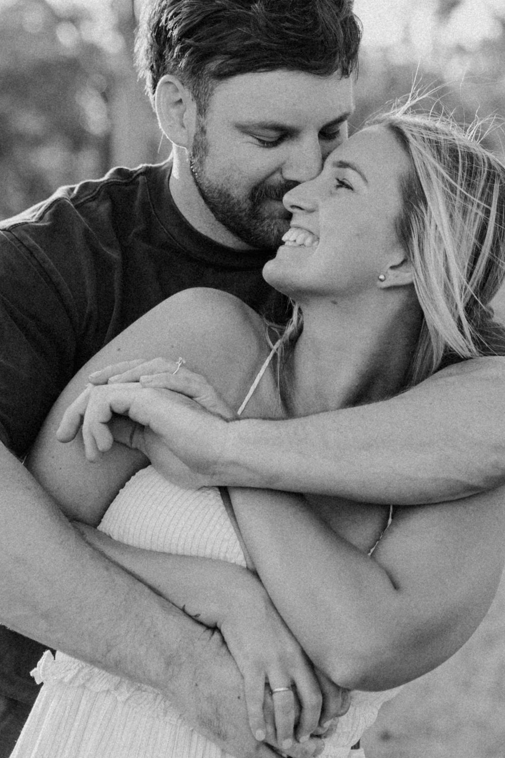 Black and white intimate portrait of couple embracing and laughing together in romantic moment outdoors.