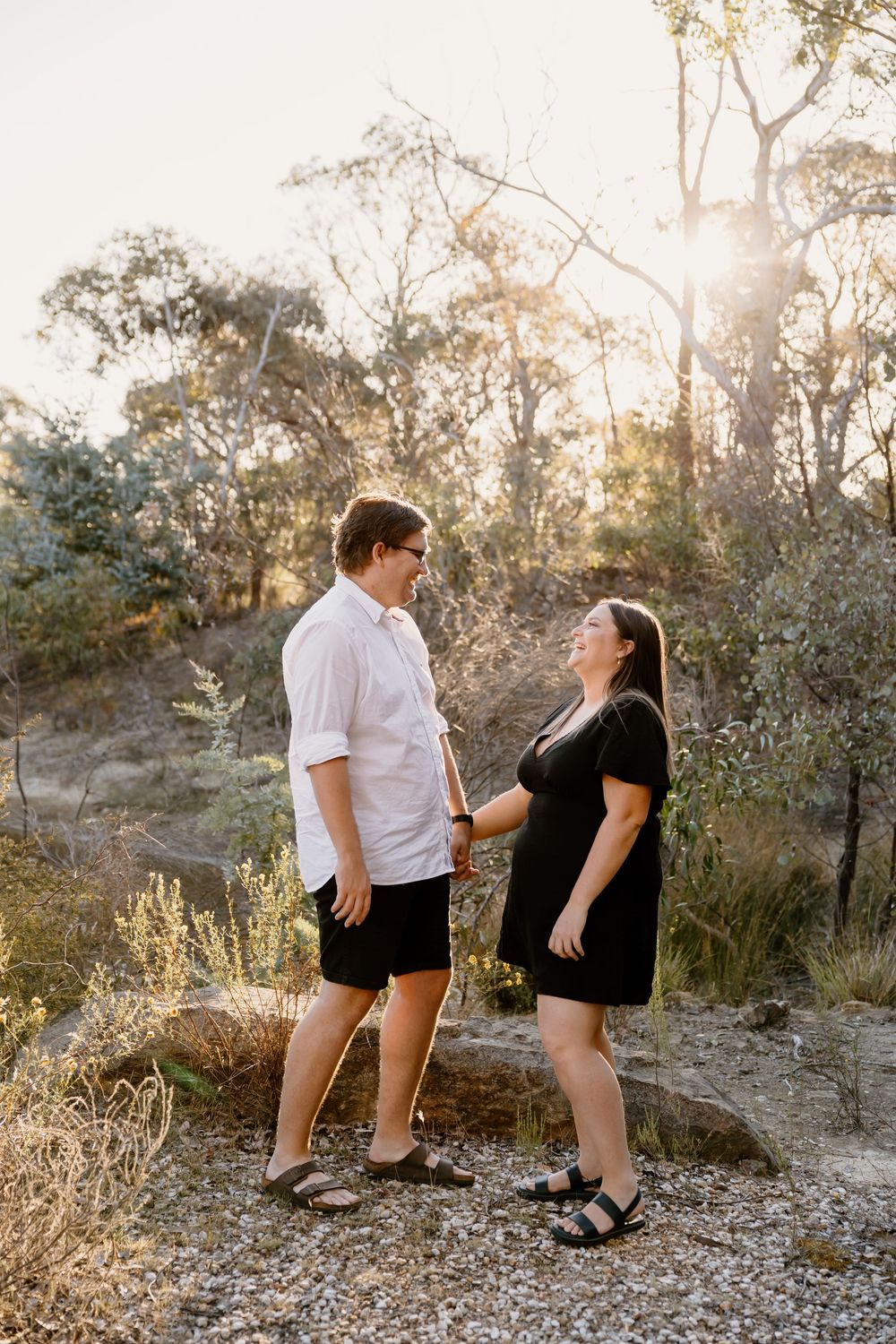 A couple stands together on a rocky path at sunset surrounded by natural Australian bushland scenery.