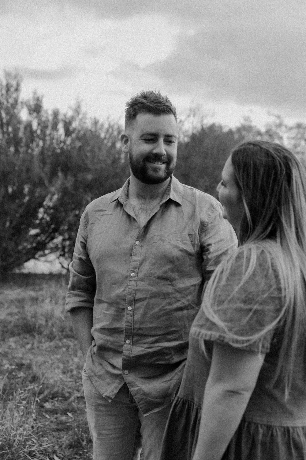 Black and white portrait of a couple sharing a romantic moment outdoors in a natural setting with trees in the background.