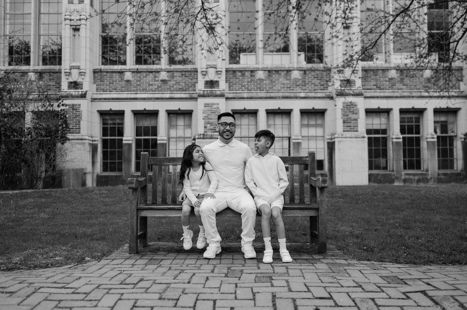 A monochromatic photograph of three people sitting together on a bench in front of a historic building facade.
