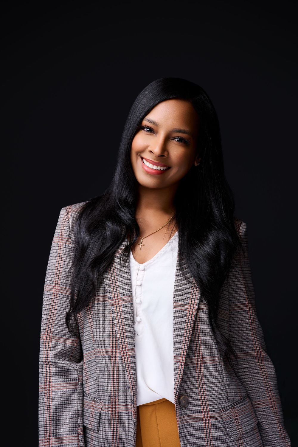 Smiling young woman with long black hair wearing a plaid blazer and white top, posing against a dark background. New Jersey headshot photos