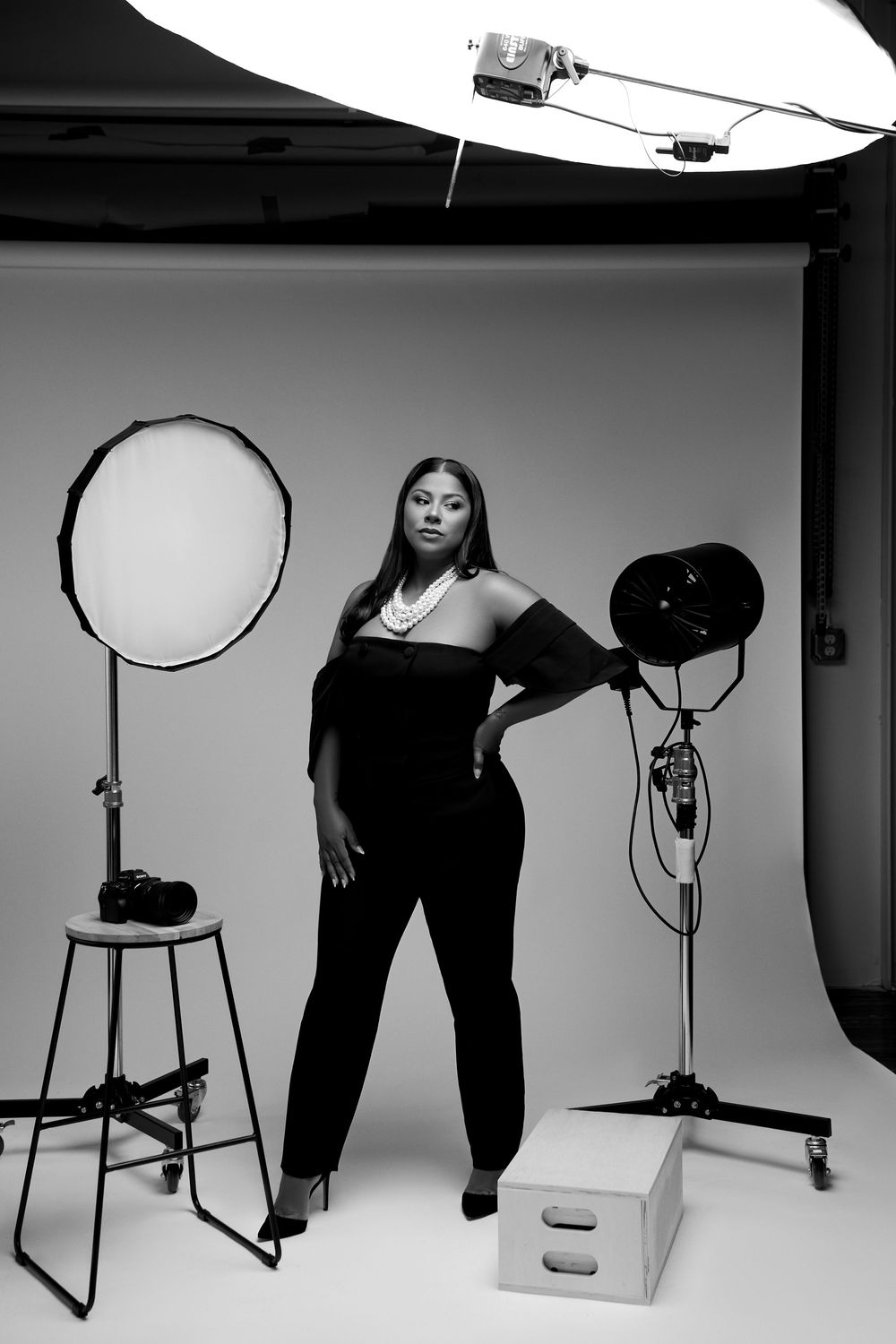 Professional photo studio setup with black and white lighting equipment, reflectors, and stool against seamless backdrop.