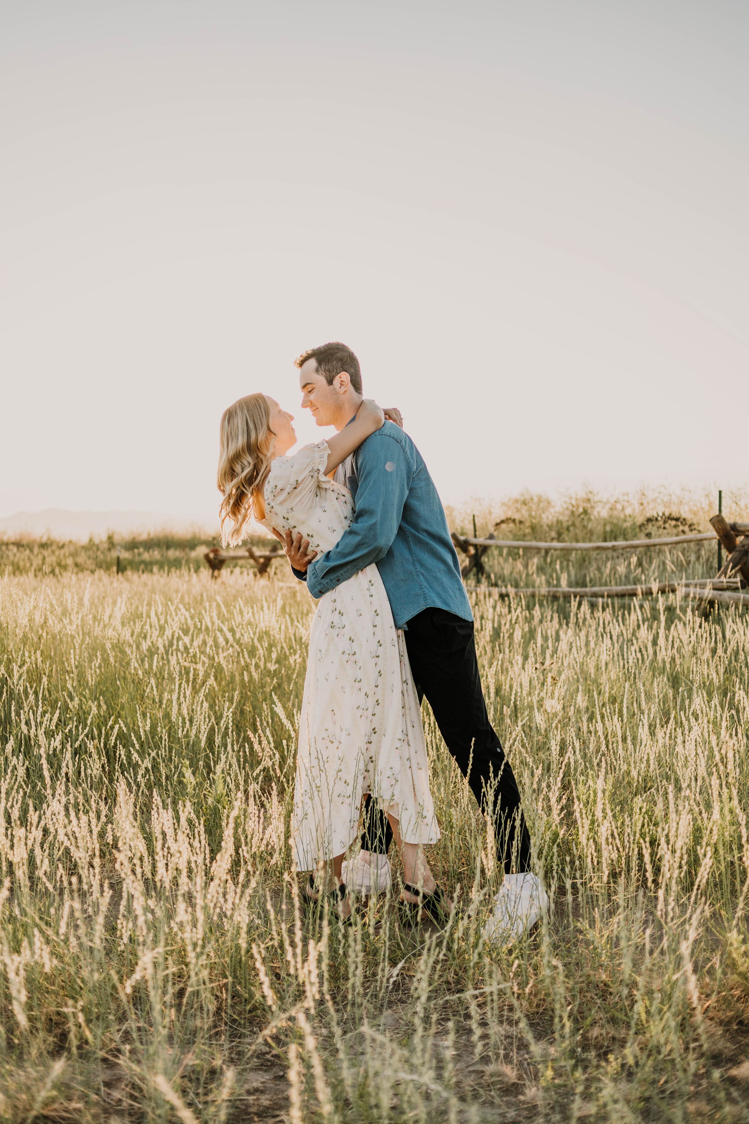 A romantic couple embraces in a sun-lit field of tall grass during golden hour.