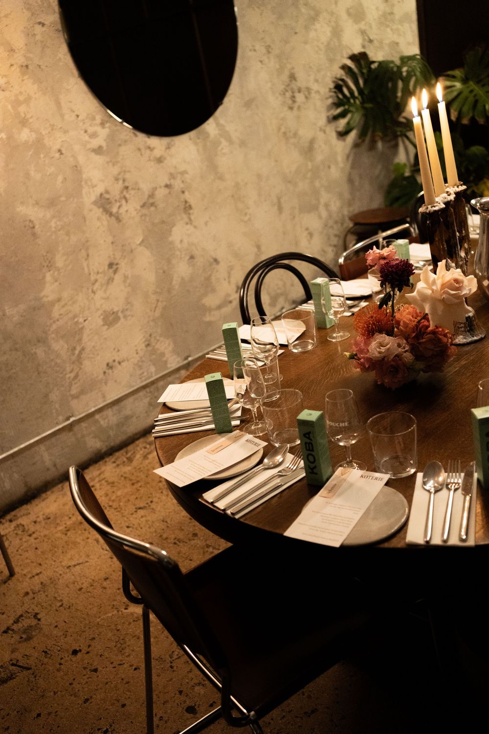 An intimate candlelit dinner table setting with white linens, glowing candles, and floral centerpieces against a rustic wall.