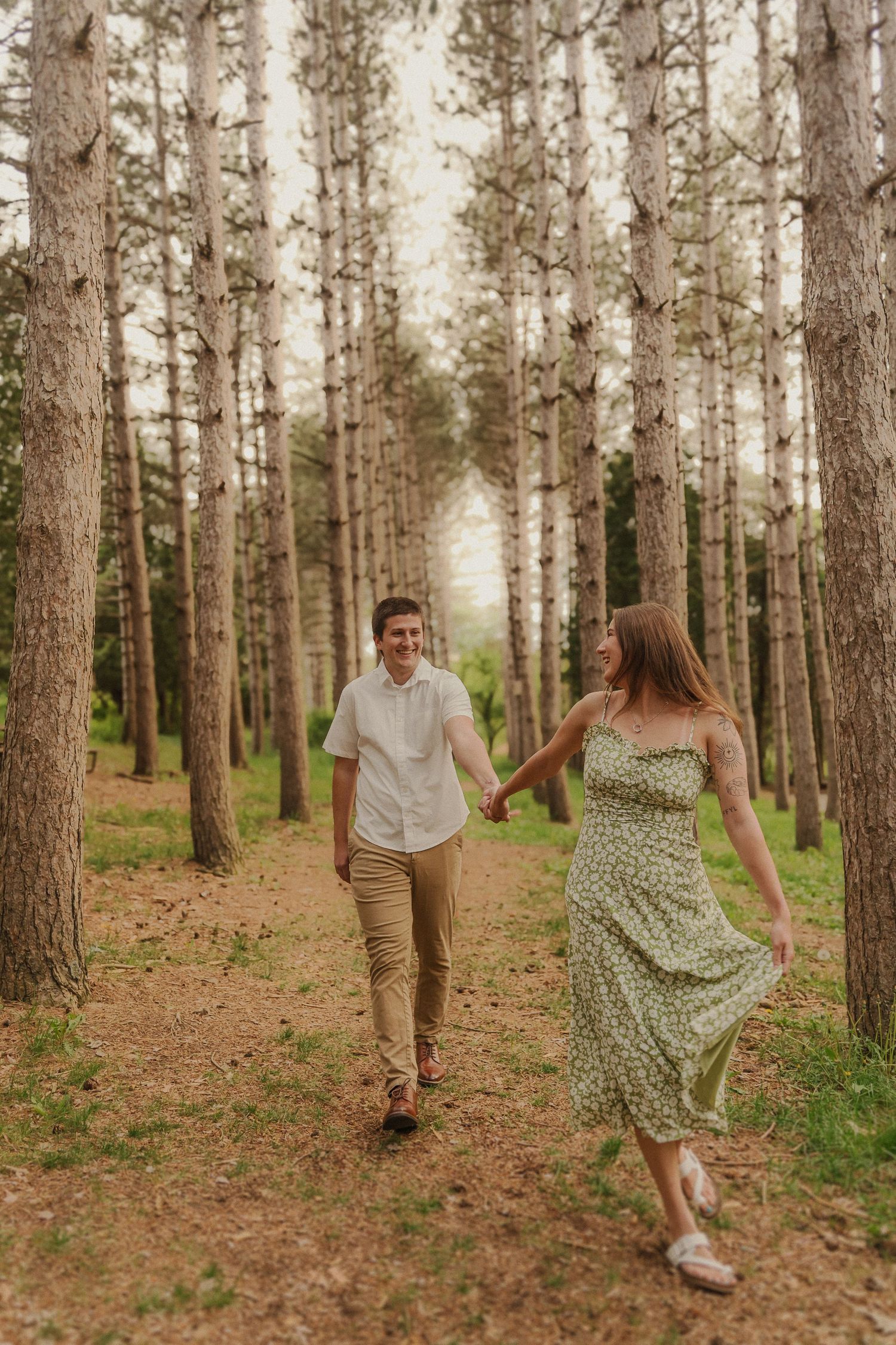 A couple holding hands while walking through a serene pine forest on a misty path.