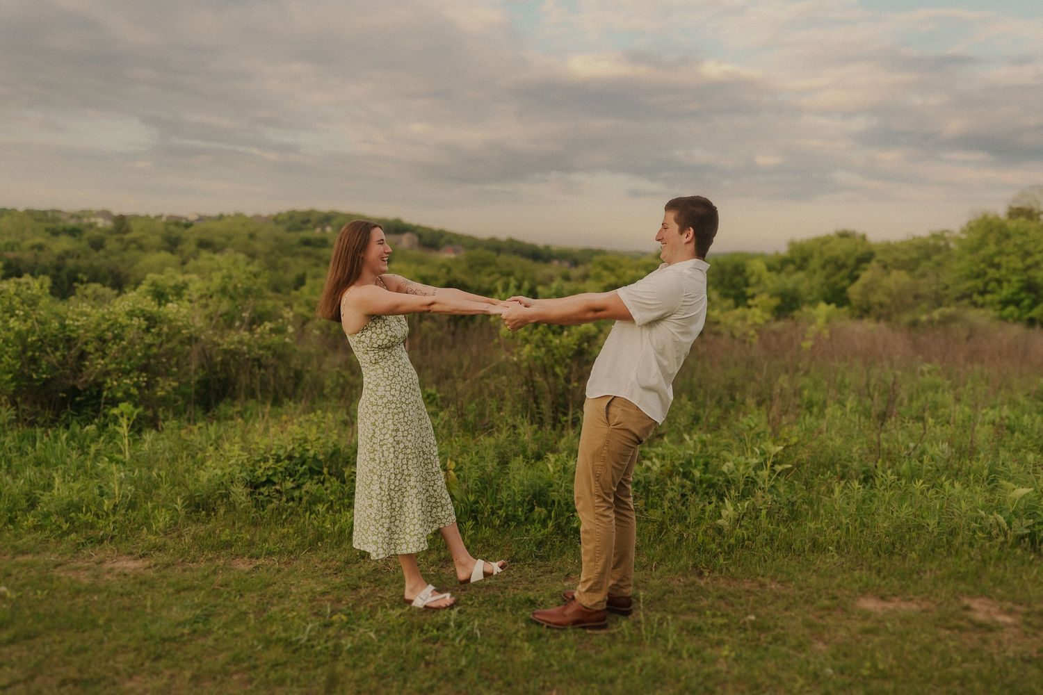 A couple in casual attire dances across a lush green hilltop meadow at sunset in a romantic sequence of photos.