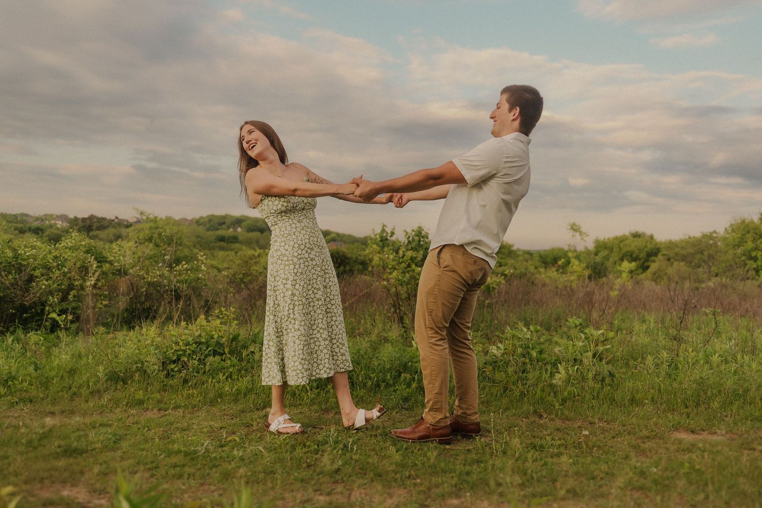Two people in casual attire dance together in a grassy meadow at sunset during summer.