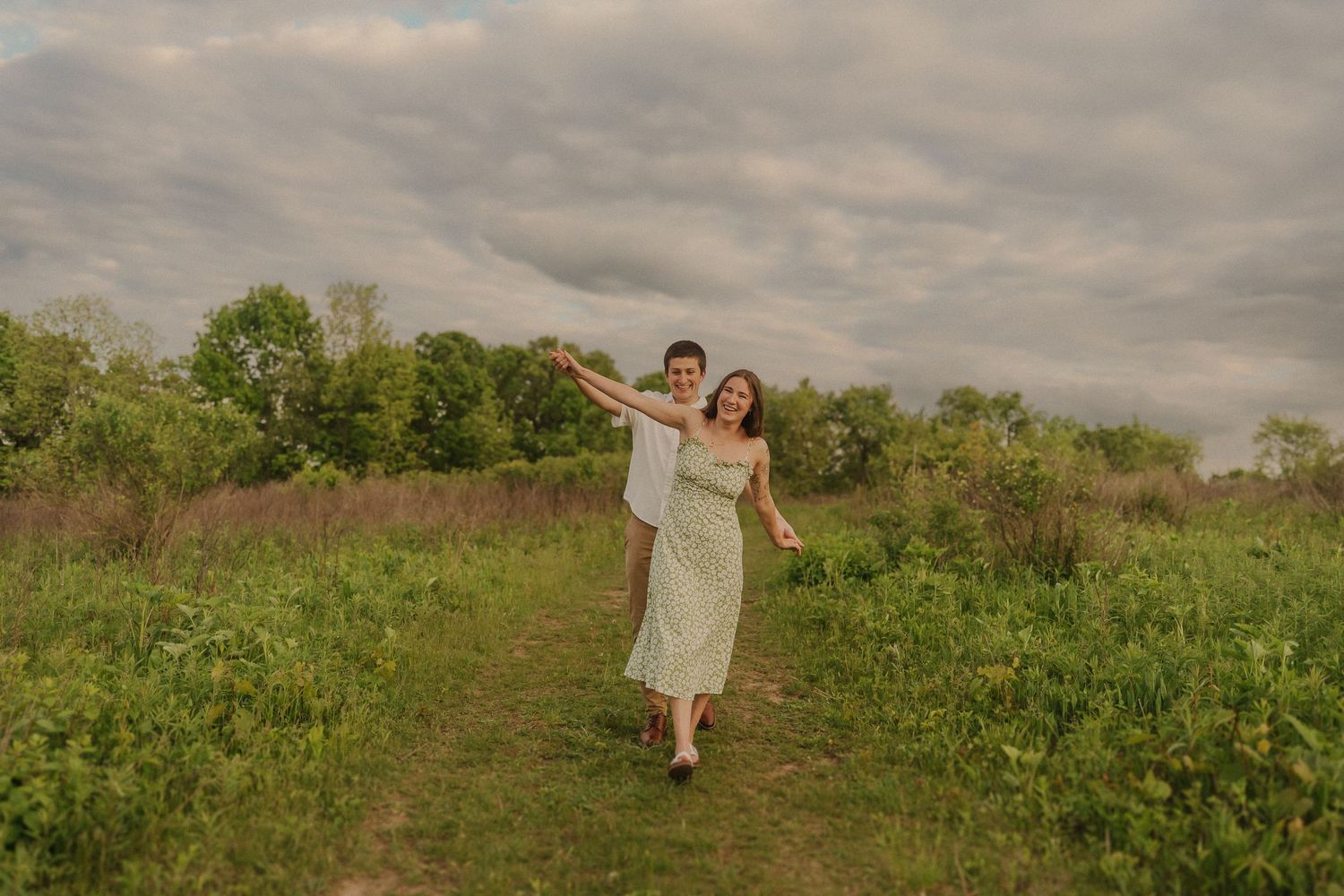 Two people enjoy a warm summer evening in a green meadow with a dramatic cloudy sky above.