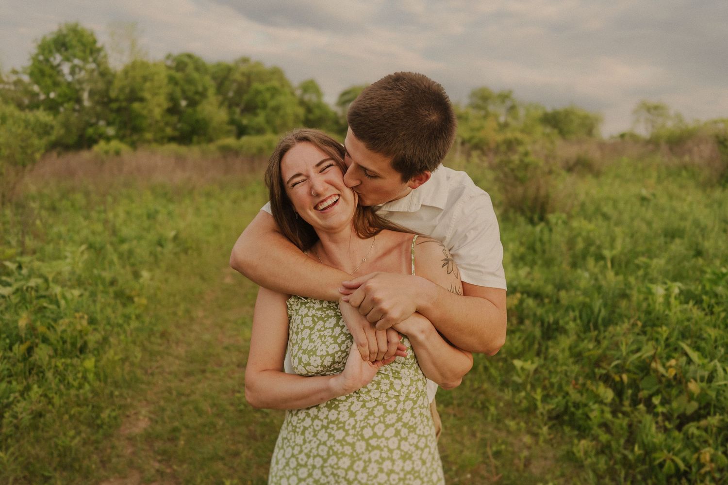 A joyful couple embraces and laughs together in a sunlit meadow during golden hour.