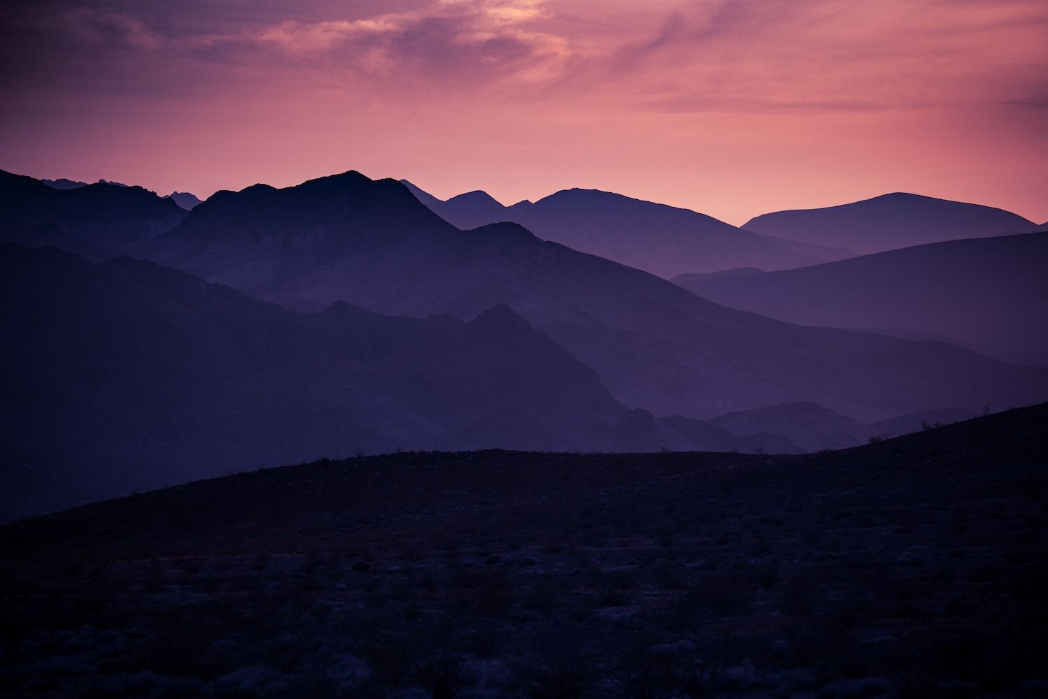 Stunning desert mountain sunset with golden orange sky and silhouetted layered mountain ranges.