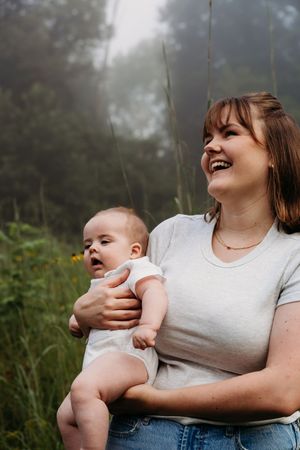 A happy moment shared outdoors in nature as parent holds smiling baby wearing white onesie.