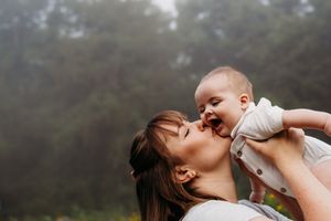 A tender moment of joy and connection between parent and baby against a misty forest backdrop.