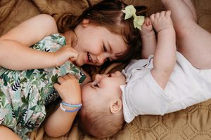 Two young children laying close together on a beige couch while smiling and playing.
