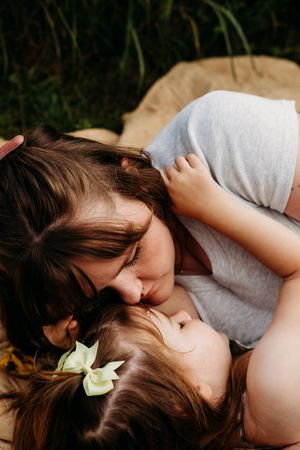 Two people share an intimate moment outdoors with a yellow flower in their hair, expressing tender affection.