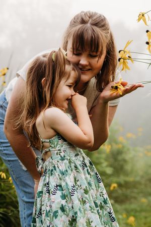 A candid outdoor scene with two people sharing a joyful moment among yellow wildflowers on a misty day.