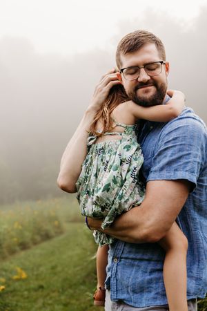 A couple embraces tenderly in a misty field with matching blue denim and floral print outfits.