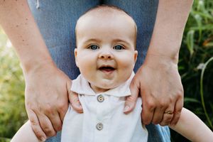 A collection of close-up photos showing hands gently holding and supporting a smiling baby wearing a white outfit.