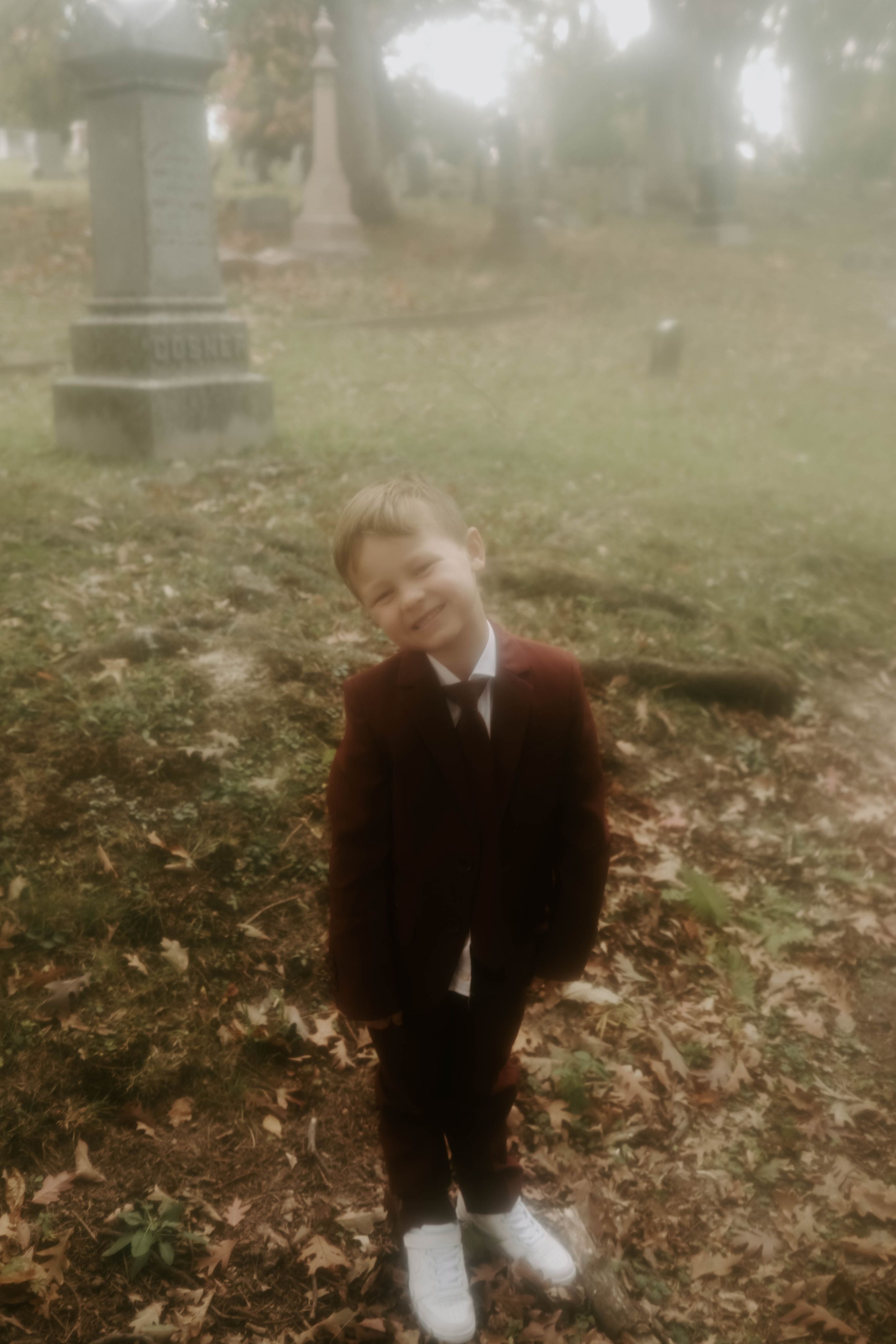 Misty cemetery scene with gravestones and fallen autumn leaves creates an eerie atmosphere.