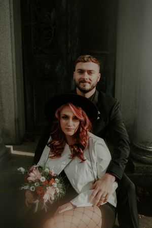 A romantic couple embraces while sitting on stone steps in moody lighting.