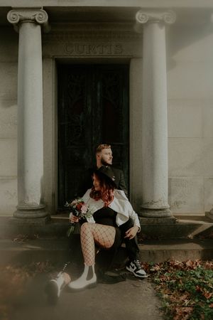 A couple sits together on stone steps surrounded by autumn leaves.