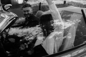 A couple shares a tender moment in black and white near a vintage car.