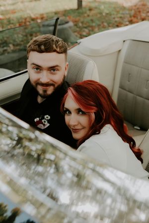 A couple smiles together while sitting in a classic car with white interior.