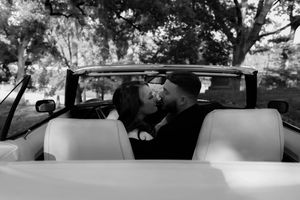 A vintage car parked under autumn trees in a moody cemetery setting.