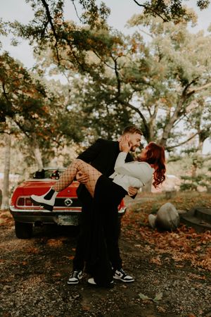 Romantic photoshoot with a couple lounging by a vintage red car surrounded by fall foliage.