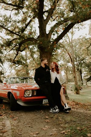 Romantic autumn photoshoot featuring a vintage red car under large oak trees.