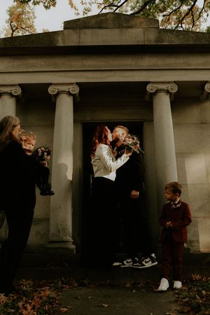 Stylish couple poses against stone columns in a cemetery during autumn.