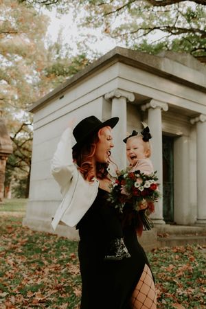 Two people in black outfits and hats pose dramatically near stone mausoleums.