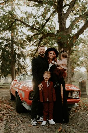 Family group portrait with a classic red car among fall trees.