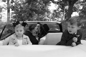 Two children peek out from a vintage car in a black and white photograph.
