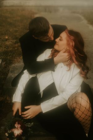 A romantic couple in black and white attire share an intimate moment on grass with autumn tones.