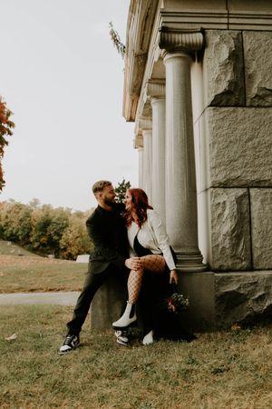 A couple embraces against classic stone columns in an autumn setting with vintage architecture.