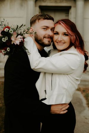 A couple in contrasting black and white outfits share an intimate moment against a stone building backdrop.