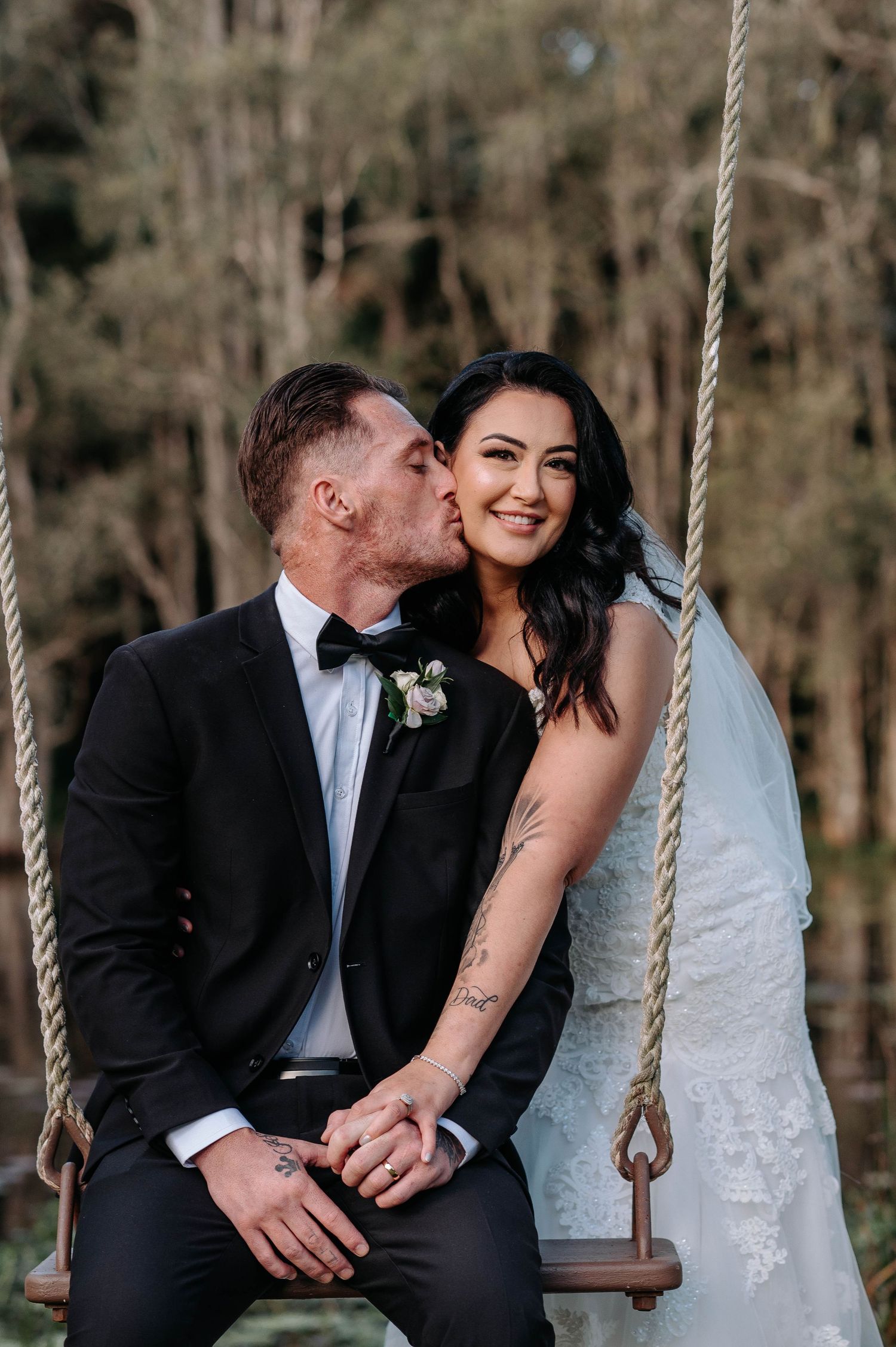 A romantic moment captured of a newlywed couple sitting together on a rustic wooden swing in a forest setting.