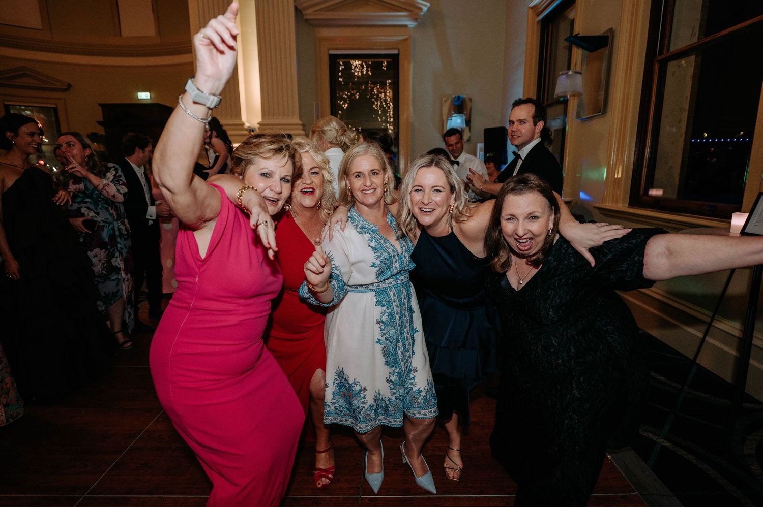 Group of friends in festive attire enjoying a lively celebration on the dance floor at an evening party.