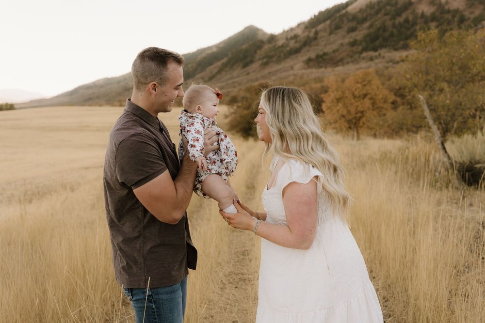 Family embracing together in golden field with mountains in background during sunset.