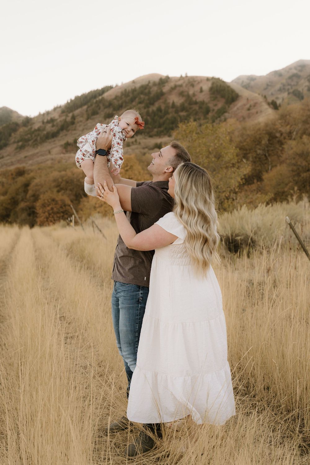 Loving family moment captured in golden field with mountains behind them.