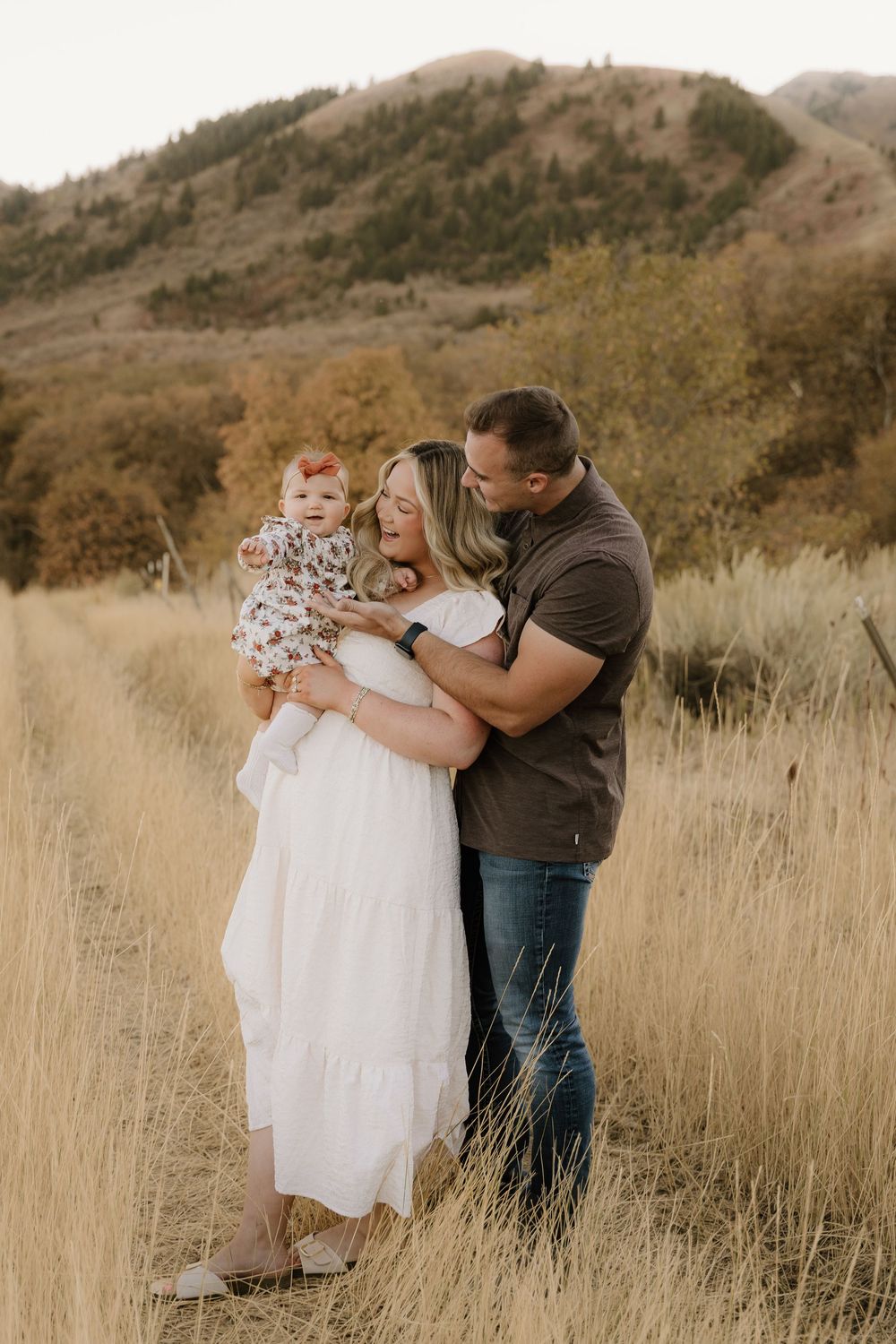 Intimate family moment captured in rustic mountain setting with tall golden grass.