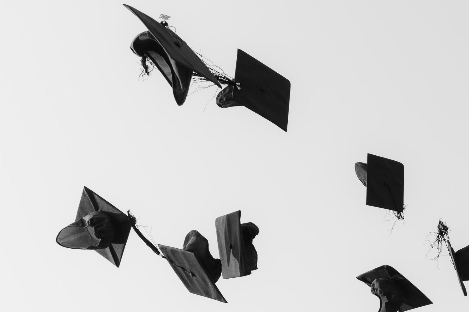 Black and white photo of graduation caps being tossed into the air against a clear sky.
