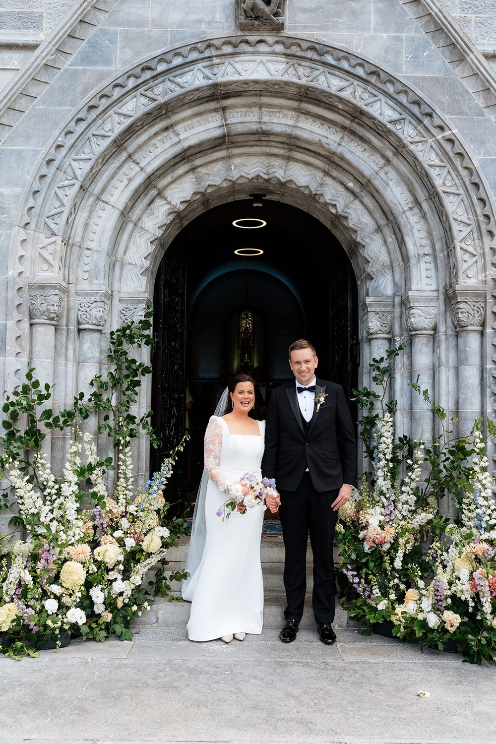 Couple exits historic stone church archway adorned with elegant white and green floral arrangements in five sequence shots.