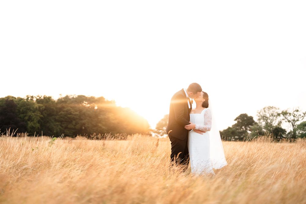 A couple stands in silhouette sharing a romantic moment in a sunlit field during golden hour.