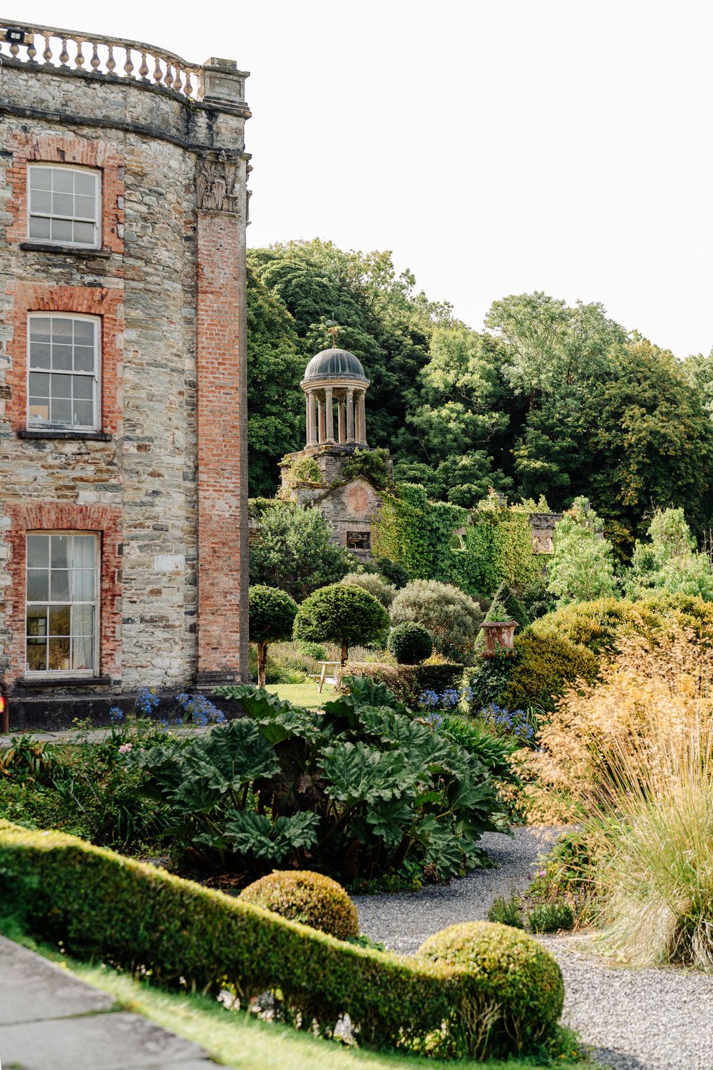 Historic stone manor house with manicured gardens featuring a classical domed gazebo and ornate landscaping details.